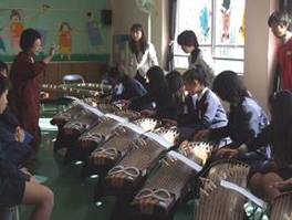 滝井小学校の児童が、 大阪音楽大学の中島名誉教授に「さくら」の琴演奏を指導してもらっている様子を写した写真