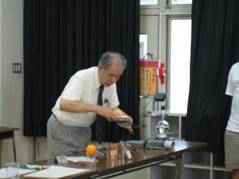 横浜国立大学の廣田名誉教授が、オレンジを使ってつくる電池について実験している様子を写した写真
