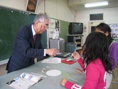 京都大学の大野名誉教授が、藤田小学校の児童の目の前でホウ酸の結晶づくりの実験を行っている様子を写した写真