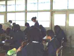 座って学習している錦中学校の生徒を見回る関西外国語大学の学生を写した写真