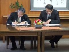 左に藤川博史教育長、右に長尾彰夫学長が座って協定書に署名する様子を写した写真