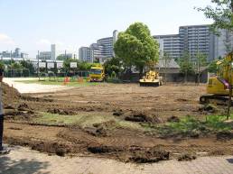 下島小学校校庭で芝生化する場所の表面の土を約10〜15センチメートル程度、黄色いショベルカーで掘り起こしている作業途中の写真