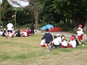 休憩時間に1年生も芝生化区域に入り、二箇所に分かれて児童が輪になって座って遊んでいる写真