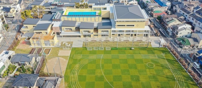 校舎、芝生が貼られたグラウンド、周りの住宅街を上空から写した写真