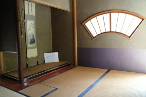 扇形の障子窓と掛け軸がかかっている床の間がある室内の写真