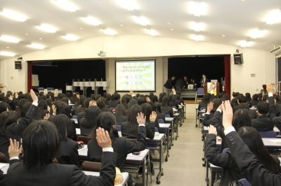 席に座っている生徒たちが挙手をしている様子を室内後方から写した写真