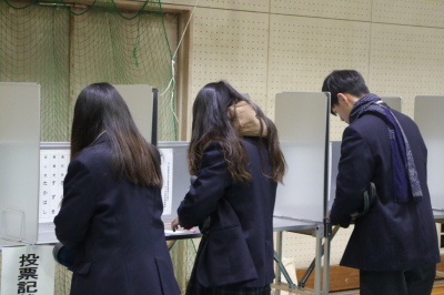 3人の生徒が投票記載台で記入をしている後ろ姿の写真