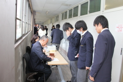 廊下にテーブルが設置され、係の職員の方が座っており、男子生徒3人が並んで受付をしている写真