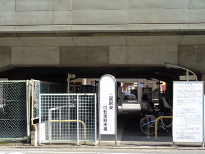 中心に土居駅東自転車駐車場と書かれた看板が立っており、出入り口右に注意書きが示された看板が立っている、土居駅東自転車駐車場の写真