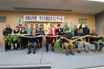 守口大根の長さコンクールで長い大根を持って記念撮影をしている参加者達の写真