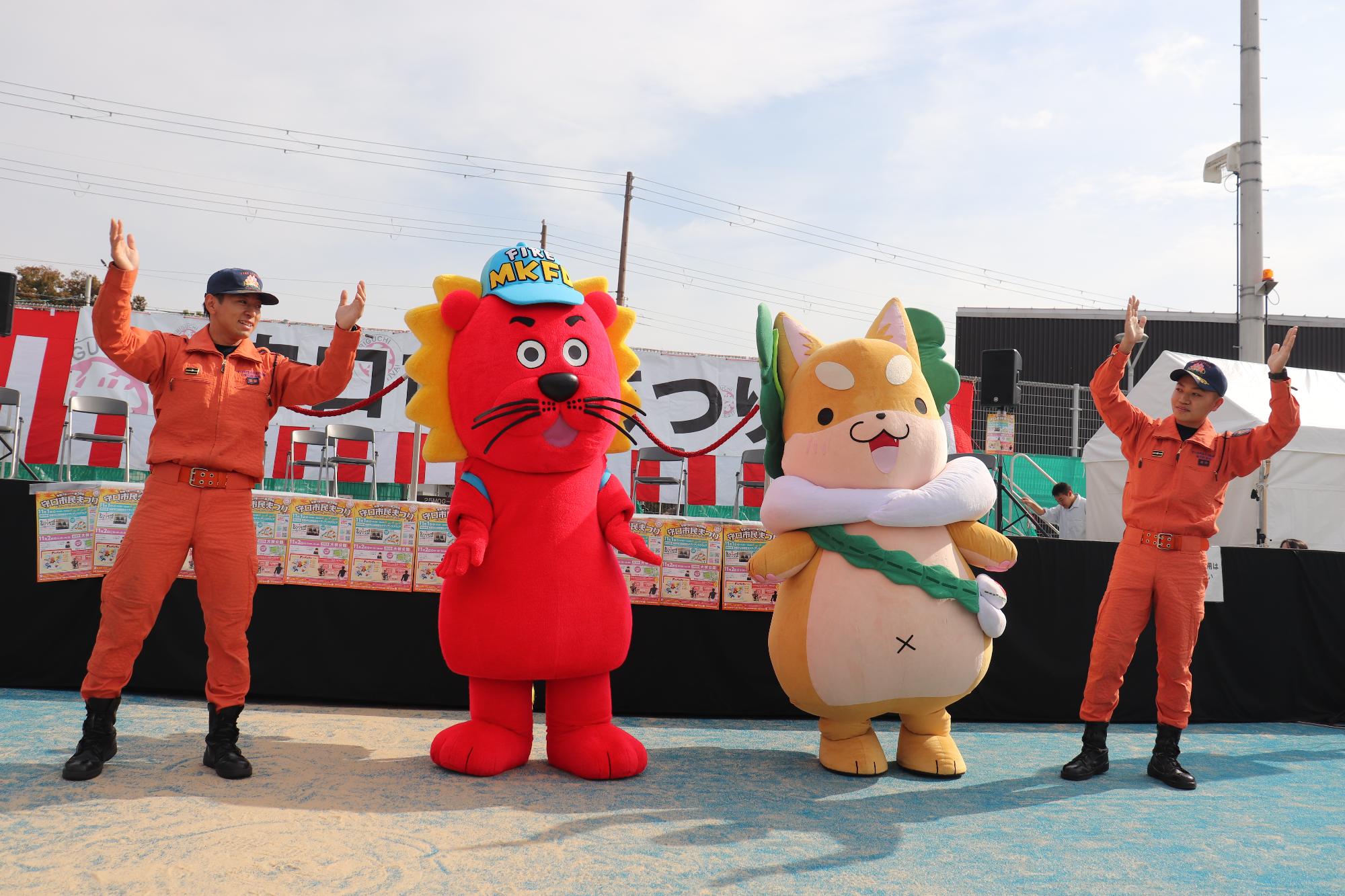 もり吉とレンダイオンと消防職員が舞台で踊っている