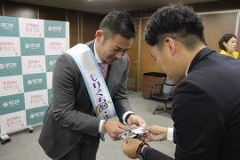 スーツを着た岩田稔さんが市の男性と名刺を交換している写真