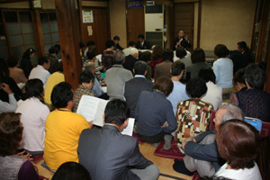 和室にたくさんの参加者の人達が座りタウンミーティングが行われている様子の写真