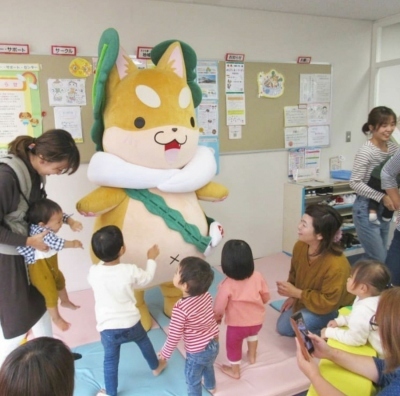 もり吉の周りに幼児とお母さん達が集まっている、市役所3階での絵本の時間の写真