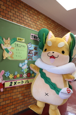 廊下にある掲示板の前に立っているもり吉の写真
