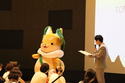 オープン記念イベントの舞台上でマイクで紹介されているもり吉の写真
