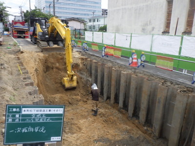 黄色の重機が穴を掘っている本町松下線築造工事発進立坑の掘削工事の施工中の写真